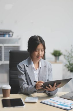 Başarılı Asyalı iş kadını dizüstü bilgisayarla gülümseyip ofisinde kahve fincanı tutuyor. Güvenilir Asyalı iş kadını ofiste mutlu mesut oturuyor..