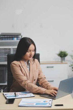 Asyalı iş kadını dizüstü bilgisayar kullanıyor ve ofiste hesap makinesi ile çalışıyor, mali raporu, iş planı yatırımını, mali analiz konseptini analiz etmeyi planlıyor..