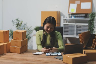 Girişim KOBİ küçük işletme girişimcisi önlük giyen Asyalı kadın dizüstü bilgisayar ve kutu kullanarak çevrimiçi müşterilere, çevrimiçi sme iş fikirlerine satış hazırlamak için siparişleri alır ve gözden geçirir.