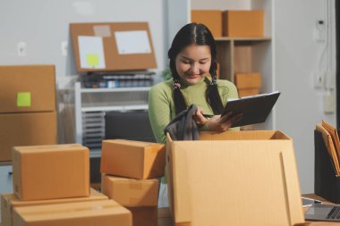 Girişim KOBİ küçük işletme girişimcisi önlük giyen Asyalı kadın dizüstü bilgisayar ve kutu kullanarak çevrimiçi müşterilere, çevrimiçi sme iş fikirlerine satış hazırlamak için siparişleri alır ve gözden geçirir.