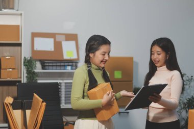 Girişim KOBİ küçük işletme girişimcisi önlük giyen Asyalı kadın dizüstü bilgisayar ve kutu kullanarak çevrimiçi müşterilere, çevrimiçi sme iş fikirlerine satış hazırlamak için siparişleri alır ve gözden geçirir.