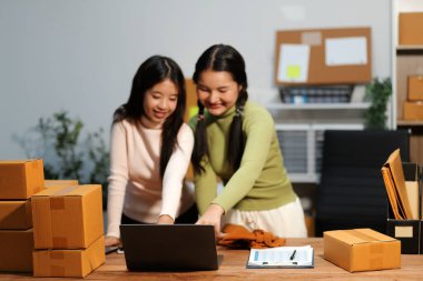 Girişim KOBİ küçük işletme girişimcisi önlük giyen Asyalı kadın dizüstü bilgisayar ve kutu kullanarak çevrimiçi müşterilere, çevrimiçi sme iş fikirlerine satış hazırlamak için siparişleri alır ve gözden geçirir.