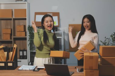 Girişim KOBİ küçük işletme girişimcisi önlük giyen Asyalı kadın dizüstü bilgisayar ve kutu kullanarak çevrimiçi müşterilere, çevrimiçi sme iş fikirlerine satış hazırlamak için siparişleri alır ve gözden geçirir.