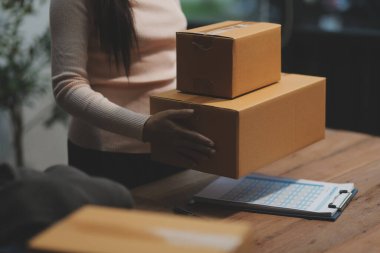 Girişim KOBİ küçük işletme girişimcisi önlük giyen Asyalı kadın dizüstü bilgisayar ve kutu kullanarak çevrimiçi müşterilere, çevrimiçi sme iş fikirlerine satış hazırlamak için siparişleri alır ve gözden geçirir.