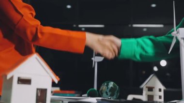 İki genç adam el sıkışıyor ve yeşil ev modeliyle bir model gösteriyor. Gayrimenkul ve emlak sigortası kavramı.