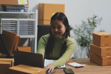 Girişim KOBİ küçük işletme girişimcisi önlük giyen Asyalı kadın dizüstü bilgisayar ve kutu kullanarak çevrimiçi müşterilere, çevrimiçi sme iş fikirlerine satış hazırlamak için siparişleri alır ve gözden geçirir.