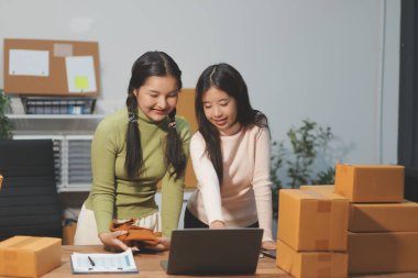 Girişim KOBİ küçük işletme girişimcisi önlük giyen Asyalı kadın dizüstü bilgisayar ve kutu kullanarak çevrimiçi müşterilere, çevrimiçi sme iş fikirlerine satış hazırlamak için siparişleri alır ve gözden geçirir.