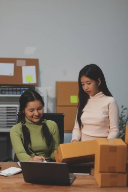 Girişim KOBİ küçük işletme girişimcisi önlük giyen Asyalı kadın dizüstü bilgisayar ve kutu kullanarak çevrimiçi müşterilere, çevrimiçi sme iş fikirlerine satış hazırlamak için siparişleri alır ve gözden geçirir.