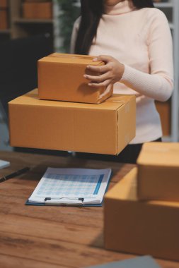 Girişim KOBİ küçük işletme girişimcisi önlük giyen Asyalı kadın dizüstü bilgisayar ve kutu kullanarak çevrimiçi müşterilere, çevrimiçi sme iş fikirlerine satış hazırlamak için siparişleri alır ve gözden geçirir.