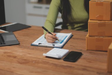 Girişim KOBİ küçük işletme girişimcisi önlük giyen Asyalı kadın dizüstü bilgisayar ve kutu kullanarak çevrimiçi müşterilere, çevrimiçi sme iş fikirlerine satış hazırlamak için siparişleri alır ve gözden geçirir.