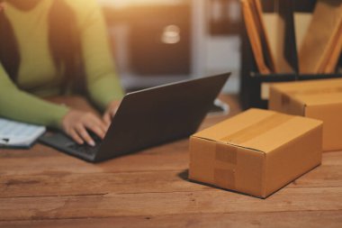 Girişim KOBİ küçük işletme girişimcisi önlük giyen Asyalı kadın dizüstü bilgisayar ve kutu kullanarak çevrimiçi müşterilere, çevrimiçi sme iş fikirlerine satış hazırlamak için siparişleri alır ve gözden geçirir.