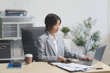 Başarılı Asyalı iş kadını dizüstü bilgisayarla gülümseyip ofisinde kahve fincanı tutuyor. Güvenilir Asyalı iş kadını ofiste mutlu mesut oturuyor..