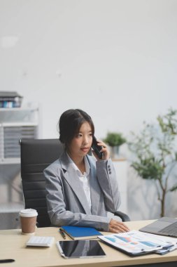 Ofisteki resmi takım elbiseli Asyalı iş kadını akıllı telefon ve çalışma süresince mutlu ve neşeli.