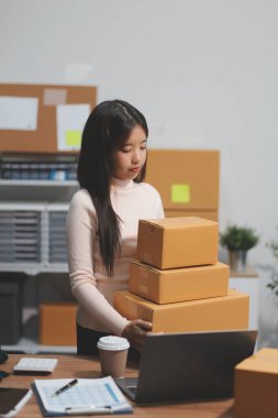 Girişim KOBİ küçük işletme girişimcisi önlük giyen Asyalı kadın dizüstü bilgisayar ve kutu kullanarak çevrimiçi müşterilere, çevrimiçi sme iş fikirlerine satış hazırlamak için siparişleri alır ve gözden geçirir.