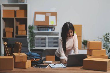 Girişim KOBİ küçük işletme girişimcisi önlük giyen Asyalı kadın dizüstü bilgisayar ve kutu kullanarak çevrimiçi müşterilere, çevrimiçi sme iş fikirlerine satış hazırlamak için siparişleri alır ve gözden geçirir.