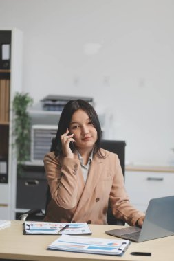 Ofisteki resmi takım elbiseli Asyalı iş kadını akıllı telefon ve çalışma süresince mutlu ve neşeli.