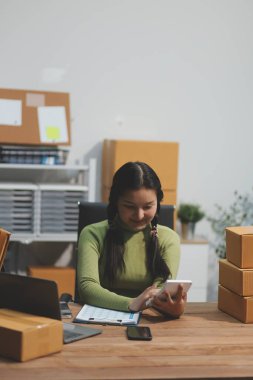 Girişim KOBİ küçük işletme girişimcisi önlük giyen Asyalı kadın dizüstü bilgisayar ve kutu kullanarak çevrimiçi müşterilere, çevrimiçi sme iş fikirlerine satış hazırlamak için siparişleri alır ve gözden geçirir.