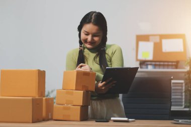 Girişim KOBİ küçük işletme girişimcisi önlük giyen Asyalı kadın dizüstü bilgisayar ve kutu kullanarak çevrimiçi müşterilere, çevrimiçi sme iş fikirlerine satış hazırlamak için siparişleri alır ve gözden geçirir.