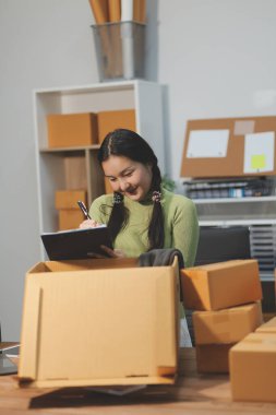 Girişim KOBİ küçük işletme girişimcisi önlük giyen Asyalı kadın dizüstü bilgisayar ve kutu kullanarak çevrimiçi müşterilere, çevrimiçi sme iş fikirlerine satış hazırlamak için siparişleri alır ve gözden geçirir.