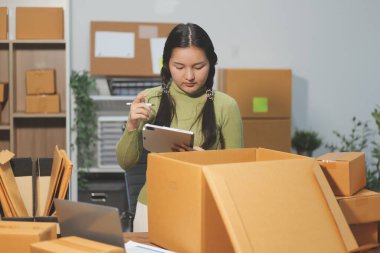 Girişim KOBİ küçük işletme girişimcisi önlük giyen Asyalı kadın dizüstü bilgisayar ve kutu kullanarak çevrimiçi müşterilere, çevrimiçi sme iş fikirlerine satış hazırlamak için siparişleri alır ve gözden geçirir.