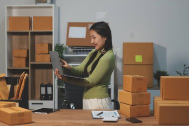 Girişim KOBİ küçük işletme girişimcisi önlük giyen Asyalı kadın dizüstü bilgisayar ve kutu kullanarak çevrimiçi müşterilere, çevrimiçi sme iş fikirlerine satış hazırlamak için siparişleri alır ve gözden geçirir.