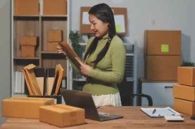 Girişim KOBİ küçük işletme girişimcisi önlük giyen Asyalı kadın dizüstü bilgisayar ve kutu kullanarak çevrimiçi müşterilere, çevrimiçi sme iş fikirlerine satış hazırlamak için siparişleri alır ve gözden geçirir.