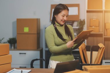 Girişim KOBİ küçük işletme girişimcisi önlük giyen Asyalı kadın dizüstü bilgisayar ve kutu kullanarak çevrimiçi müşterilere, çevrimiçi sme iş fikirlerine satış hazırlamak için siparişleri alır ve gözden geçirir.