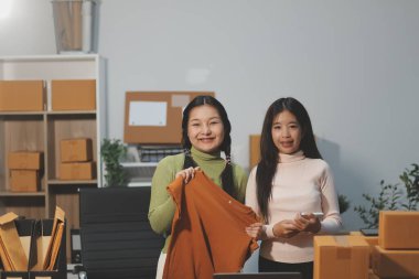 Girişim KOBİ küçük işletme girişimcisi önlük giyen Asyalı kadın dizüstü bilgisayar ve kutu kullanarak çevrimiçi müşterilere, çevrimiçi sme iş fikirlerine satış hazırlamak için siparişleri alır ve gözden geçirir.