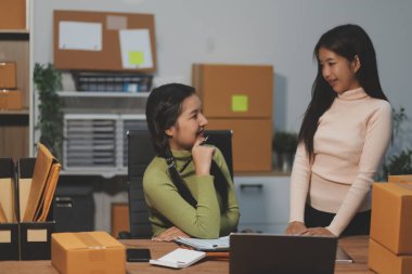 Girişim KOBİ küçük işletme girişimcisi önlük giyen Asyalı kadın dizüstü bilgisayar ve kutu kullanarak çevrimiçi müşterilere, çevrimiçi sme iş fikirlerine satış hazırlamak için siparişleri alır ve gözden geçirir.