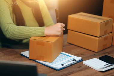 Girişim KOBİ küçük işletme girişimcisi önlük giyen Asyalı kadın dizüstü bilgisayar ve kutu kullanarak çevrimiçi müşterilere, çevrimiçi sme iş fikirlerine satış hazırlamak için siparişleri alır ve gözden geçirir.