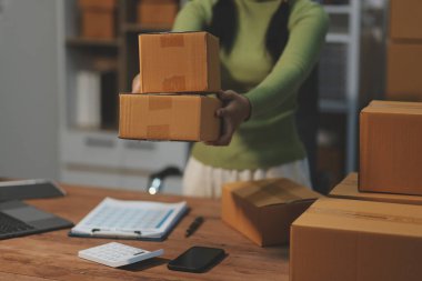 Girişim KOBİ küçük işletme girişimcisi önlük giyen Asyalı kadın dizüstü bilgisayar ve kutu kullanarak çevrimiçi müşterilere, çevrimiçi sme iş fikirlerine satış hazırlamak için siparişleri alır ve gözden geçirir.