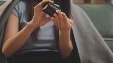 Kadın oturma odasında koltukta otururken cep telefonu kullanıyor.