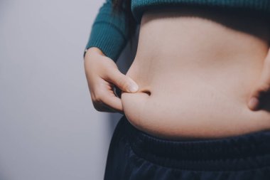 Asyalı kadın sol eliyle karnını çimdikliyor.