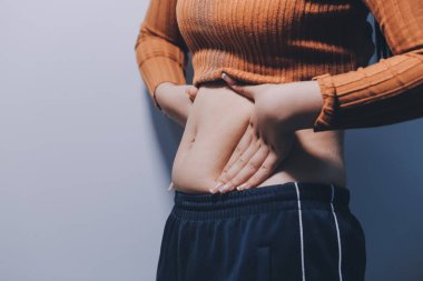 Asyalı kadın sol eliyle karnını çimdikliyor.