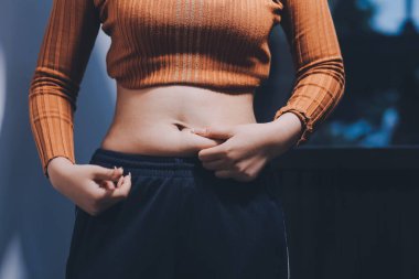 Asyalı kadın sol eliyle karnını çimdikliyor.