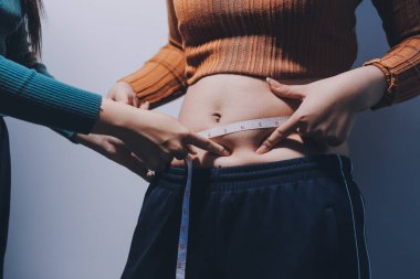 Asyalı kadın sol eliyle karnını çimdikliyor.