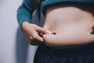 Asyalı kadın sol eliyle karnını çimdikliyor.