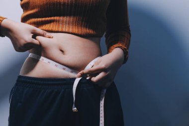 Asyalı kadın sol eliyle karnını çimdikliyor.