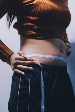 Asyalı kadın sol eliyle karnını çimdikliyor.