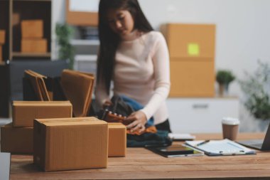 Girişim KOBİ küçük işletme girişimcisi önlük giyen Asyalı kadın dizüstü bilgisayar ve kutu kullanarak çevrimiçi müşterilere, çevrimiçi sme iş fikirlerine satış hazırlamak için siparişleri alır ve gözden geçirir.