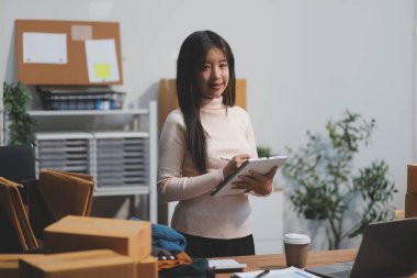 Girişim KOBİ küçük işletme girişimcisi önlük giyen Asyalı kadın dizüstü bilgisayar ve kutu kullanarak çevrimiçi müşterilere, çevrimiçi sme iş fikirlerine satış hazırlamak için siparişleri alır ve gözden geçirir.