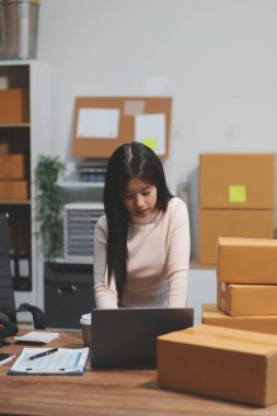 Girişim KOBİ küçük işletme girişimcisi önlük giyen Asyalı kadın dizüstü bilgisayar ve kutu kullanarak çevrimiçi müşterilere, çevrimiçi sme iş fikirlerine satış hazırlamak için siparişleri alır ve gözden geçirir.