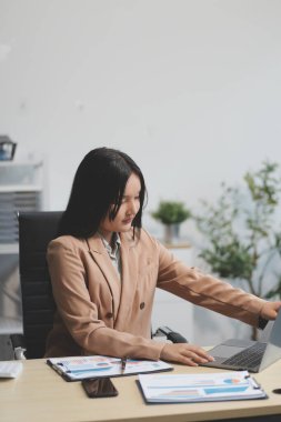Asyalı iş kadını dizüstü bilgisayar kullanıyor ve ofiste hesap makinesi ile çalışıyor, mali raporu, iş planı yatırımını, mali analiz konseptini analiz etmeyi planlıyor..