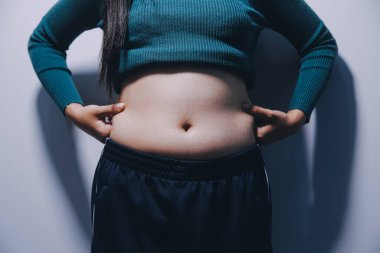 Asyalı kadın sol eliyle karnını çimdikliyor.