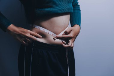 Asyalı kadın sol eliyle karnını çimdikliyor.