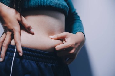 Asyalı kadın sol eliyle karnını çimdikliyor.