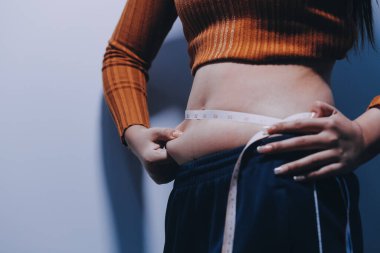 Asyalı kadın sol eliyle karnını çimdikliyor.