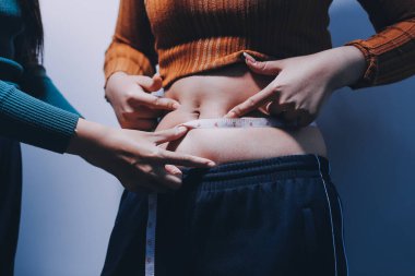 Asyalı kadın sol eliyle karnını çimdikliyor.