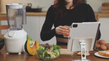 Genç bir kadın akıllı telefonu mutfakta smoothie yapmak için kullanıyor. sağlıklı yiyecekler.
