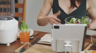 Kadın akıllı telefon kullanıyor ve mutfakta taze sebze salatası yapıyor..